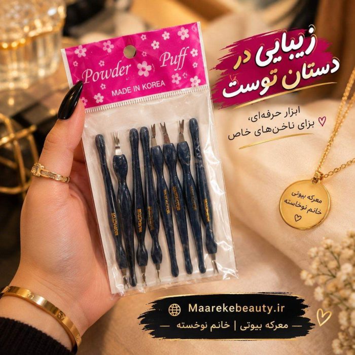 تصویری از گوشت گیر ناخن Powder Puff در بسته‌بندی پلاستیکی پلمپ شده که توسط یک دست با لاک مشکی نگهداری می‌شود و گردنبند و دکوراسیون در پس‌زمینه قرار دارند.