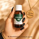 بطری شیشه‌ای ۶۰ سی‌سی روغن بادام تلخ معرکه بیوتی در دست با ناخن‌های مشکی